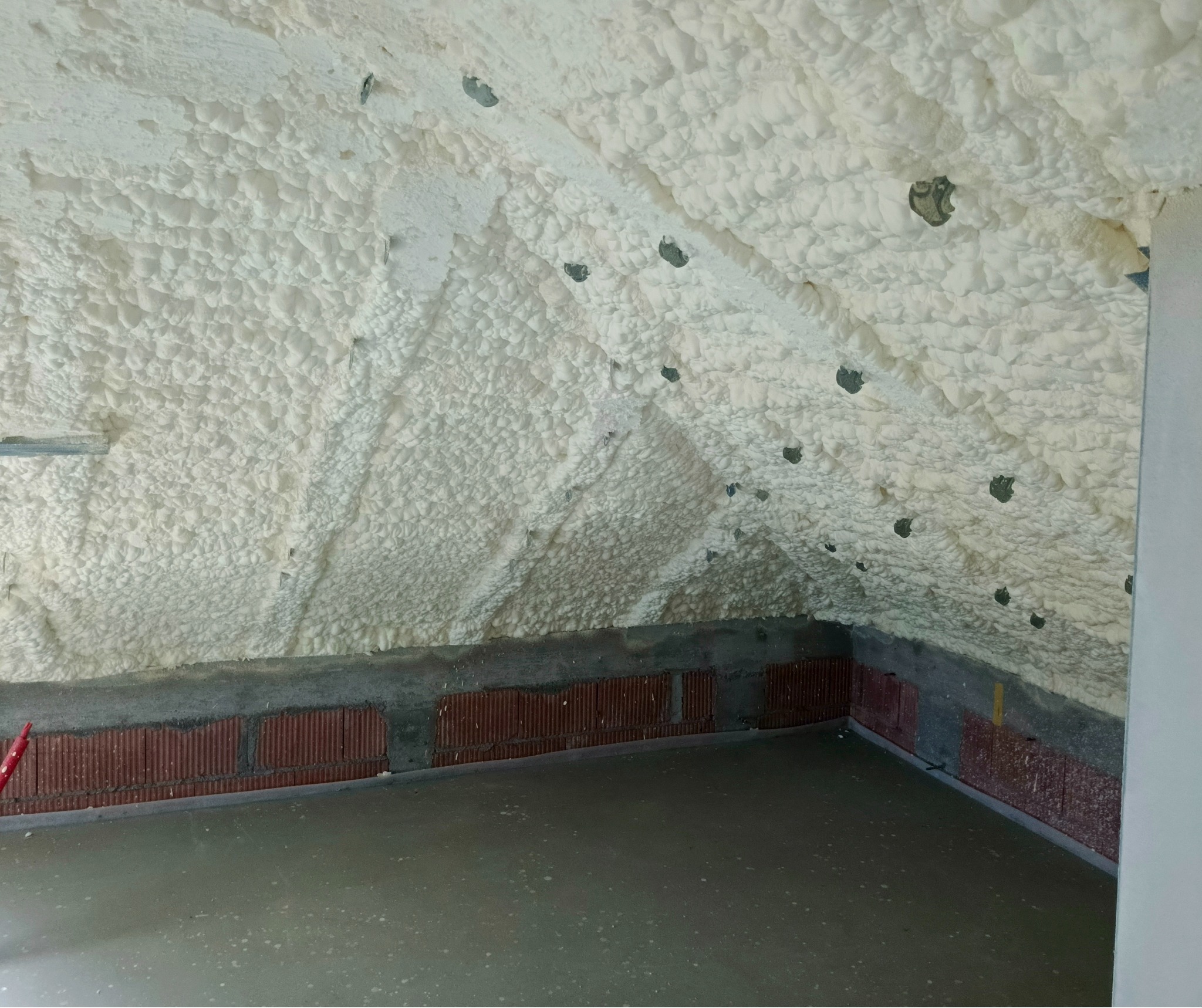 Poddasze po ociepleniu pianką PUR, widoczne równomierne pokrycie pianą na skośnych ścianach i suficie, z widocznymi elementami mocującymi.