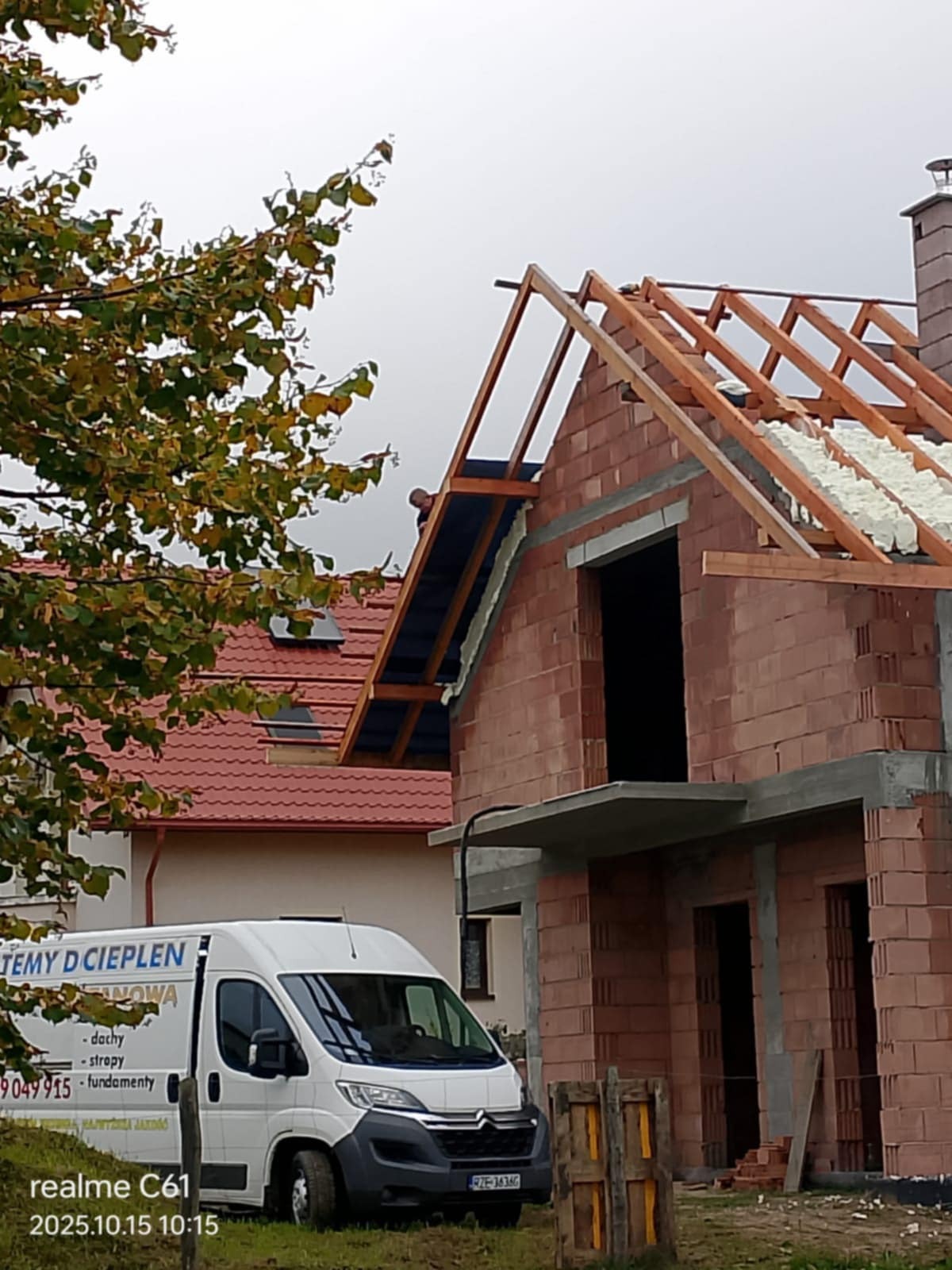 Budowa domu z ociepleniem pianką PUR na dachu, widoczna konstrukcja więźby i fragment ocieplenia. Na pierwszym planie firmowy bus z reklamą ociepleń.