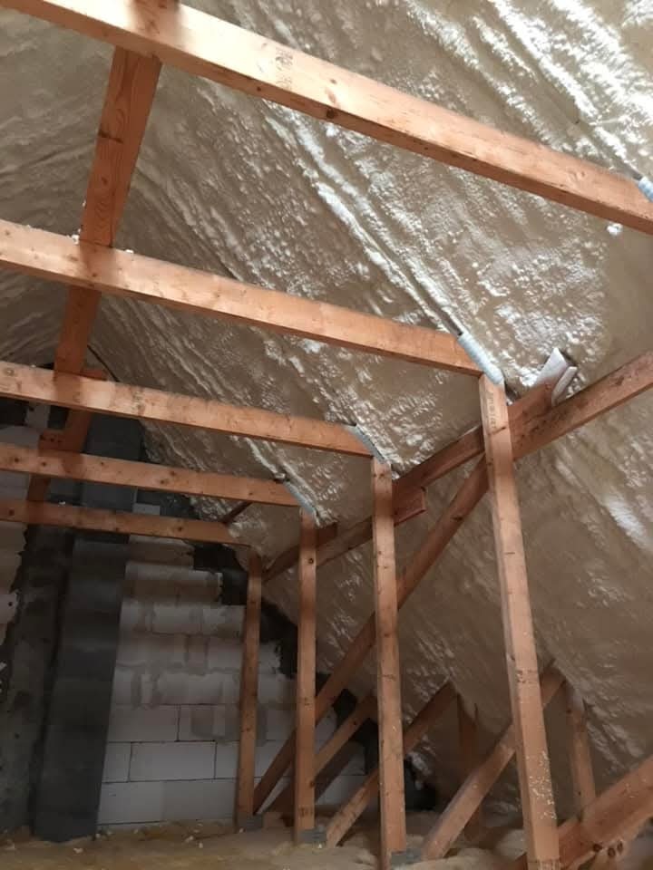 Ocieplone pianką PUR poddasze z drewnianą konstrukcją więźby dachowej. Widoczne bloki betonowe na ścianie szczytowej. Izolacja natryskowa w kolorze kremowym.