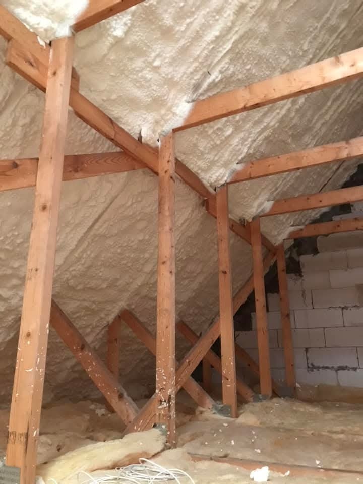 Poddasze z drewnianą konstrukcją krokwiową, wypełnione białą pianką izolacyjną. Widoczne fragmenty muru z bloczków. Na podłodze resztki pianki i przewody.