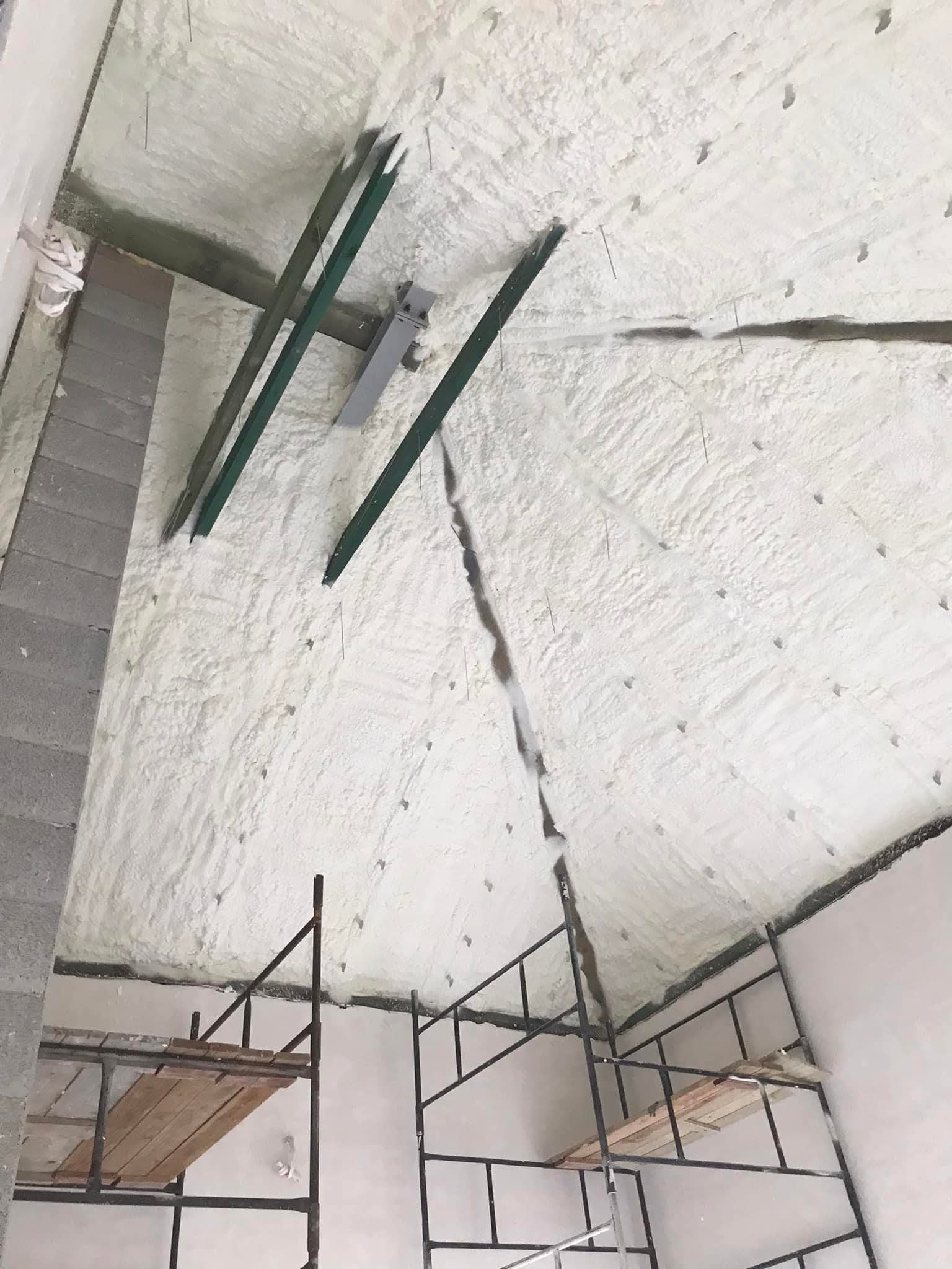 Poddasze po natrysku pianki PUR, widoczne metalowe profile i rusztowanie. Biała, nierówna powierzchnia izolacji z widocznymi punktami mocowania.