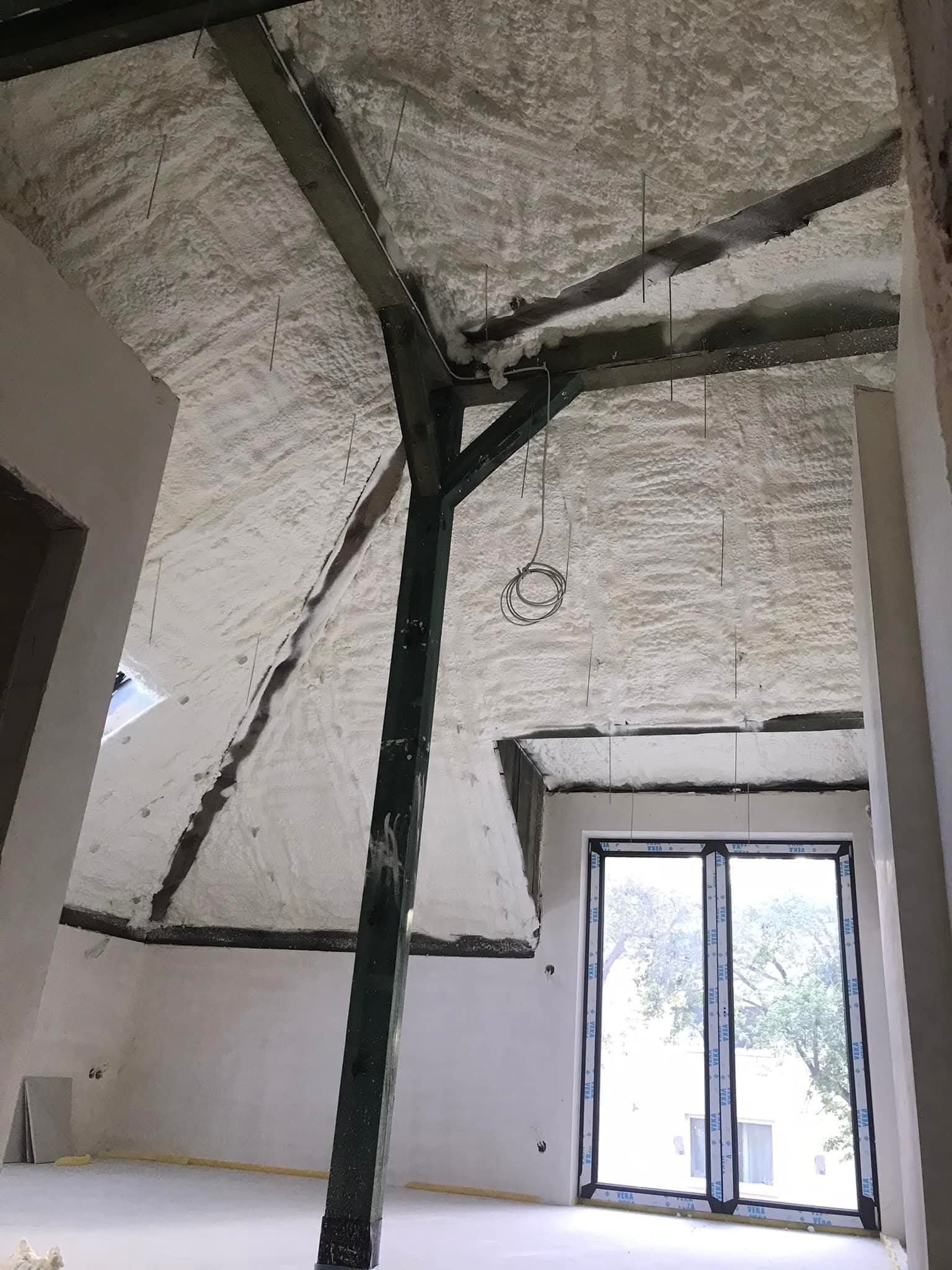 Poddasze po ociepleniu pianką PUR, widoczne drewniane elementy konstrukcyjne i okno. Biała, równomierna warstwa izolacji pokrywa skośne powierzchnie.