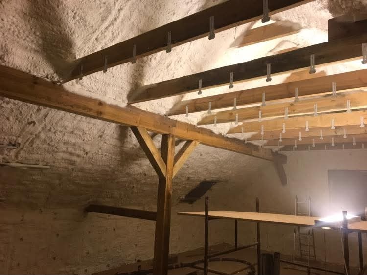 Poddasze z drewnianą konstrukcją i zaaplikowaną pianą izolacyjną, widoczne elementy mocujące. Oświetlenie podkreśla strukturę piany.