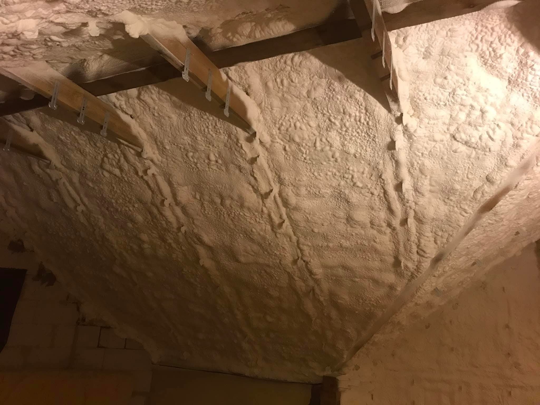 Poddasze po ociepleniu pianką PUR, widoczne drewniane elementy konstrukcyjne i równomierna warstwa izolacji. Detal: plastikowe uchwyty mocujące na belkach.