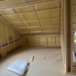 Mariusz - Szkielet domu w trakcie budowy: drewniana konstrukcja z izolacją z wełny mineralnej, widoczne elementy mocujące i fragment podłogi z materiałami izolacyjnymi.