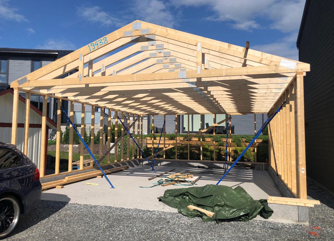 Konstrukcja szkieletowa w Lipno, widok z zewnątrz. Drewniane elementy połączone metalowymi płytkami, niebieskie podpory stabilizują konstrukcję. Widoczne fundamenty.