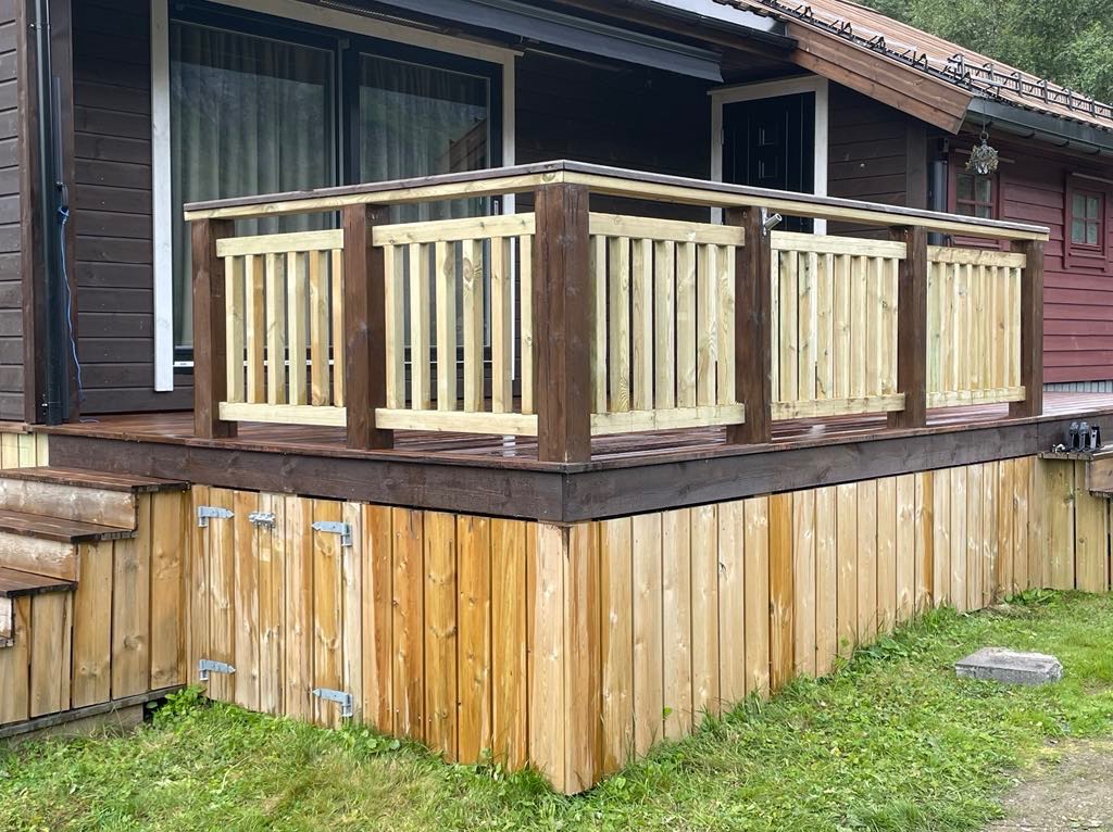 Drewniany taras z balustradą i schodami, wykończony w dwóch odcieniach brązu i naturalnym kolorze drewna, z widocznymi zawiasami na dolnej części obudowy.