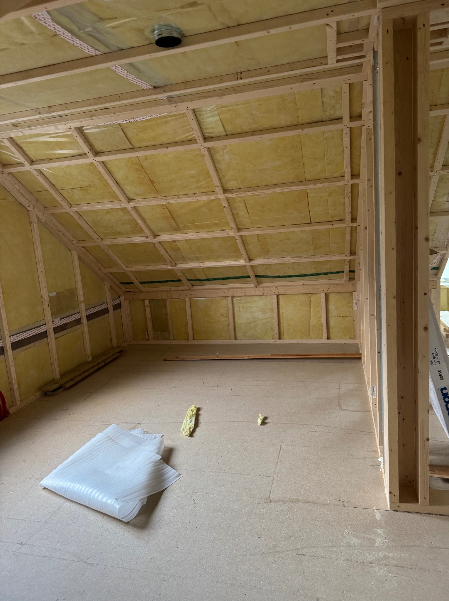 Szkielet domu w trakcie budowy: drewniana konstrukcja z izolacją z wełny mineralnej, widoczne elementy mocujące i fragment podłogi z materiałami izolacyjnymi.