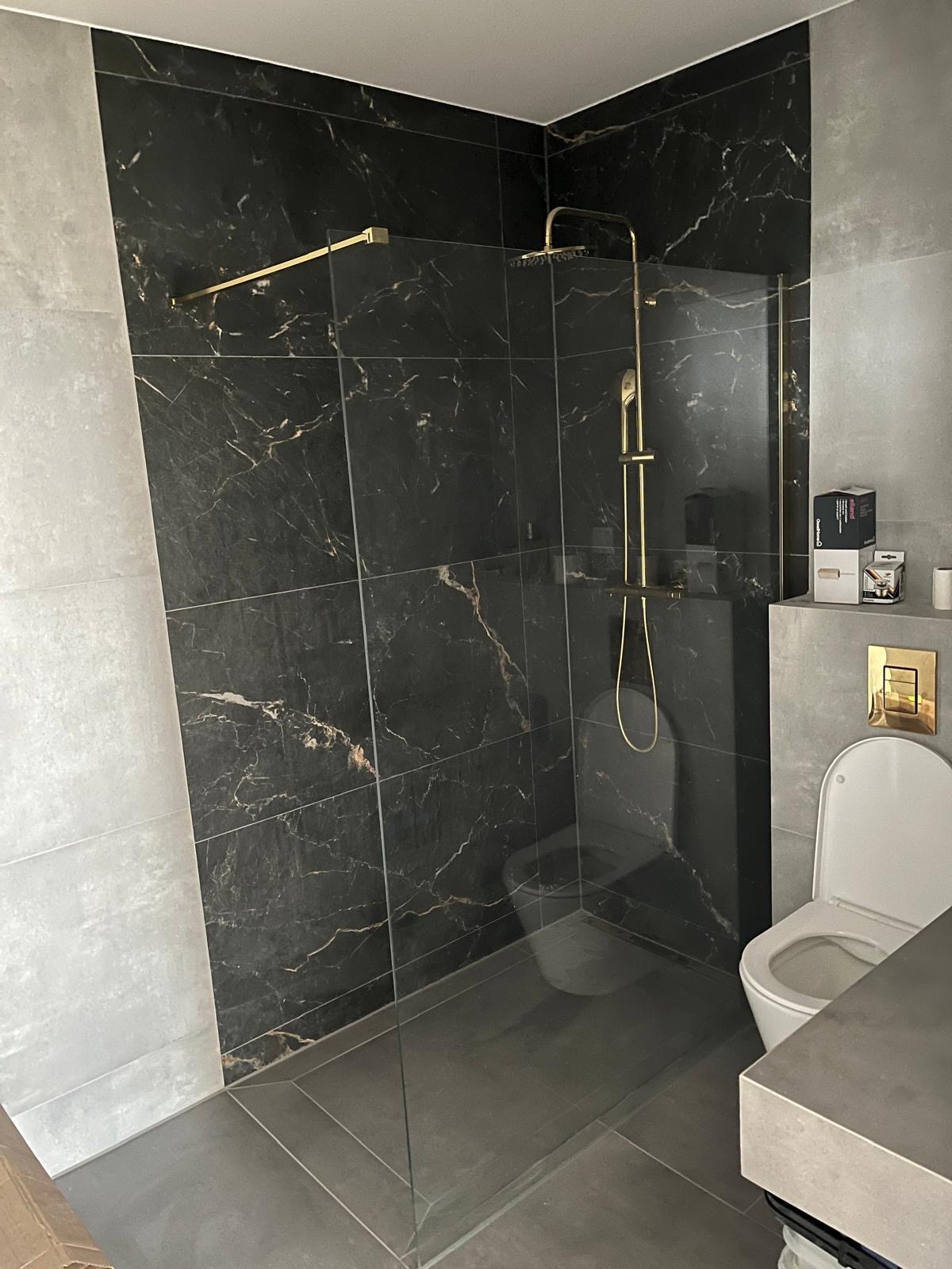 Nowoczesna kabina prysznicowa typu walk-in z czarnymi płytkami imitującymi marmur i złotą armaturą w łazience w Mełgwi. Minimalistyczny design.