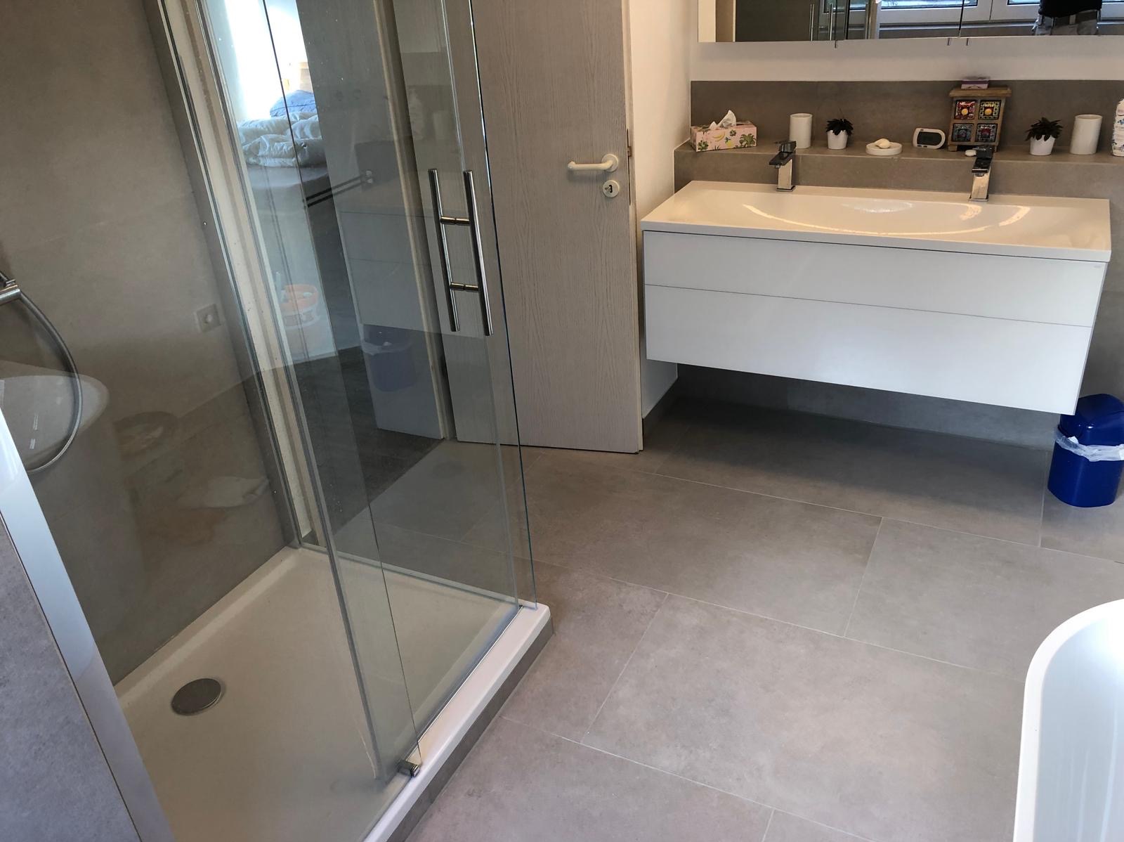 Nowoczesna łazienka z kabiną prysznicową, podwójną umywalką z szafką i szarą płytką podłogową. Minimalistyczny design, jasne wnętrze.