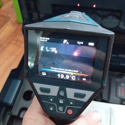 Audyt -Energia - Termowizor w dłoni, ekran pokazuje temperaturę powierzchni 19.9°C. Widoczne ustawienia daty i godziny. W tle otwarte pudełko narzędziowe.