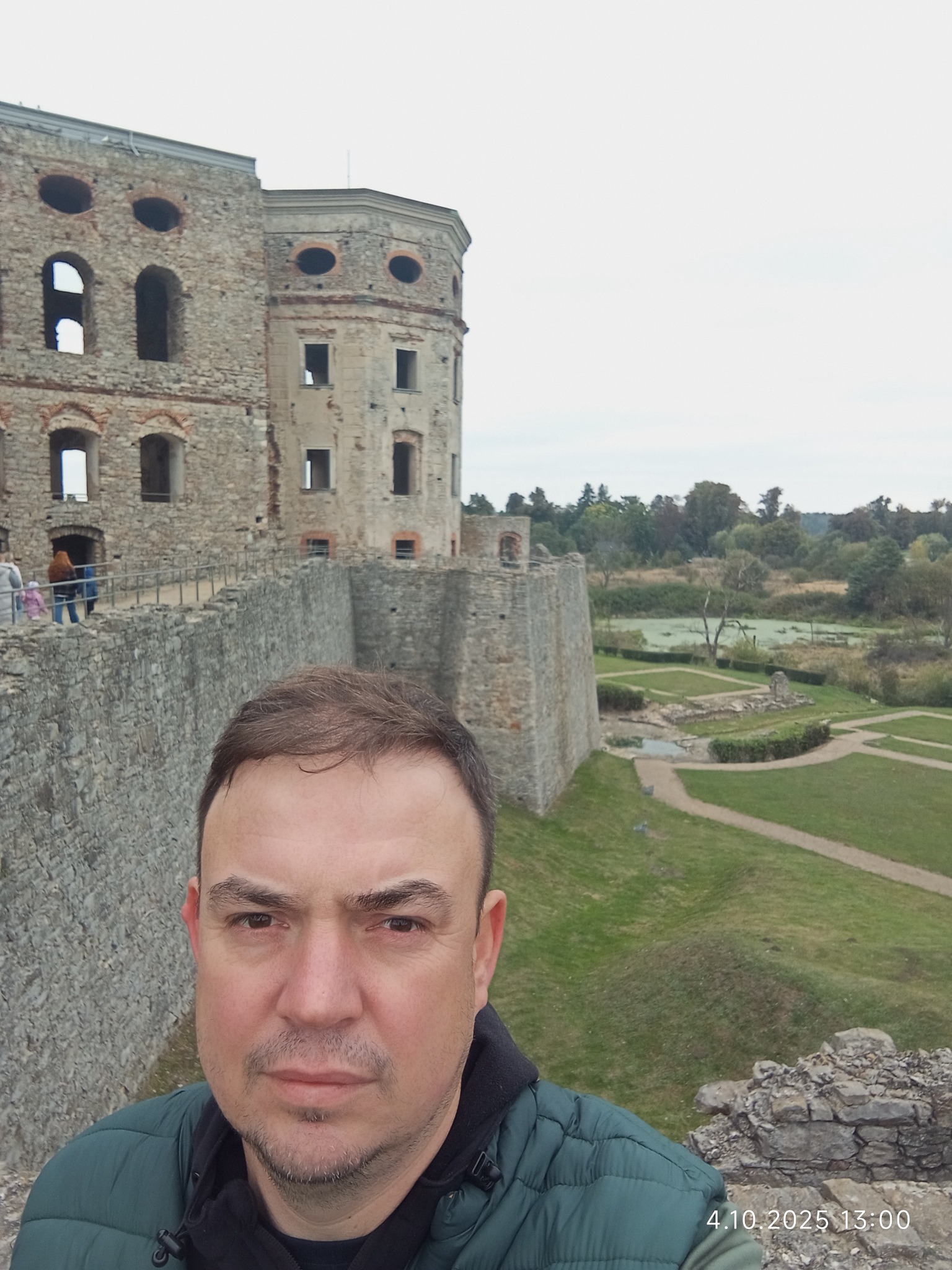 Selfie na tle ruin zamku Krzyżtopór w Ujeździe. Widoczny fragment muru, zieleń i fragment sylwetki osoby. Data i godzina w prawym dolnym rogu.
