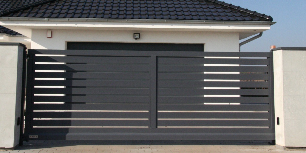 Nowoczesna, przesuwna brama w kolorze grafitowym z poziomymi szczebelkami, zamontowana przed białym budynkiem z ciemnym dachem. Minimalistyczny design, symetryczny układ.