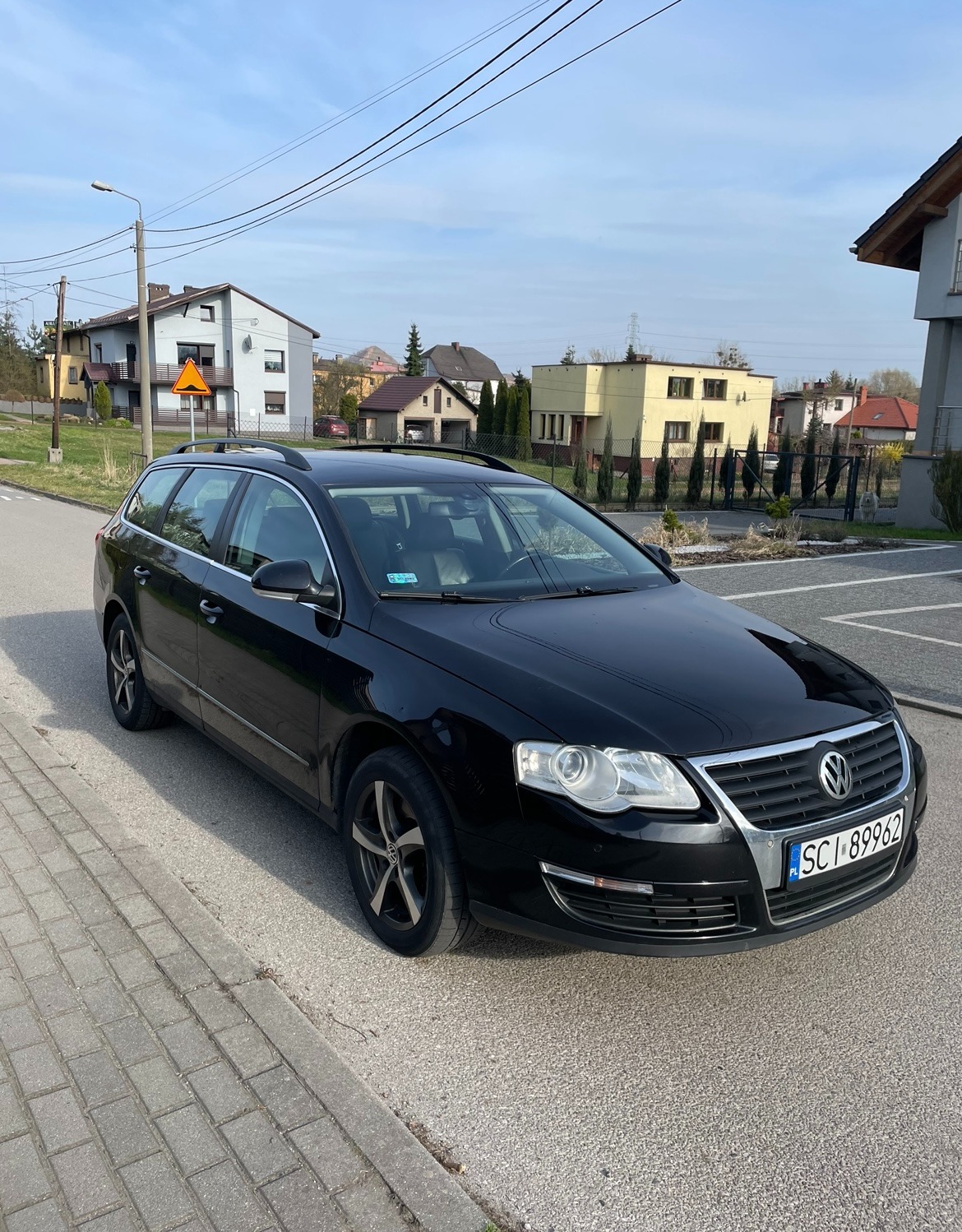 Czarny Volkswagen Passat Variant na ulicy, z widocznym numerem rejestracyjnym i elementami otoczenia, takimi jak budynki i znak drogowy.