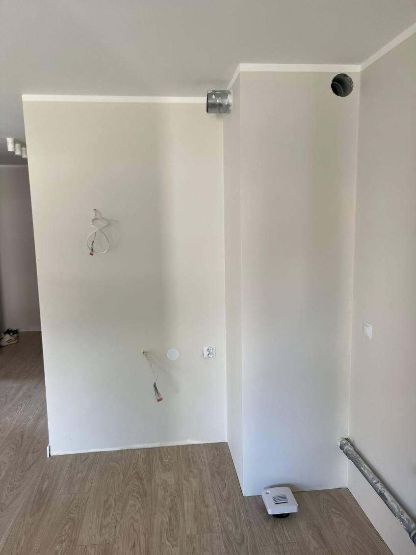 Świeżo pomalowane, jasne ściany z widocznymi instalacjami w Chorzowie. Podłoga wyłożona panelami. Widoczne otwory wentylacyjne i wystające przewody.