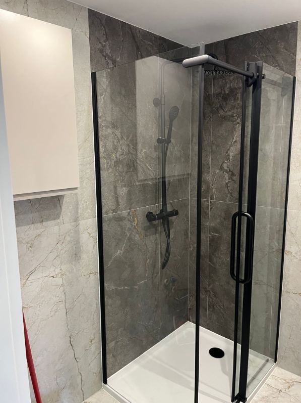 Nowoczesna kabina prysznicowa z czarnymi profilami i marmurowymi płytkami w łazience. Biała szafka wisząca po lewej stronie. Minimalistyczny design.