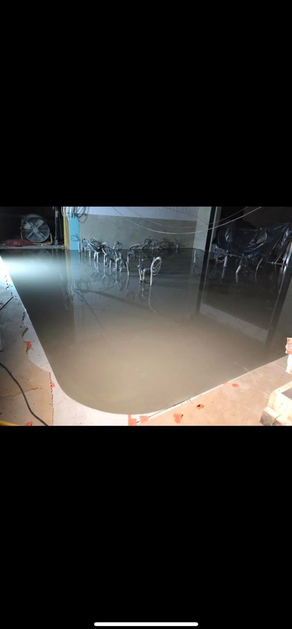 Wylana, mokra wylewka samopoziomująca na podłodze w pomieszczeniu. Widoczne narzędzia i akcesoria do rozprowadzania masy. Oświetlenie górne.