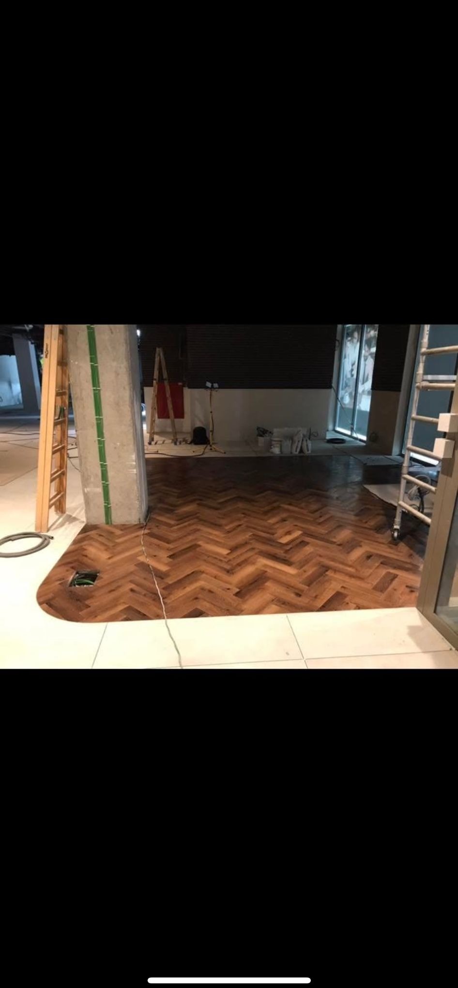 Ułożony parkiet w jodełkę na podłodze w pomieszczeniu w trakcie prac wykończeniowych. Widoczne drabiny i narzędzia. Nietypowy kształt parkietu.