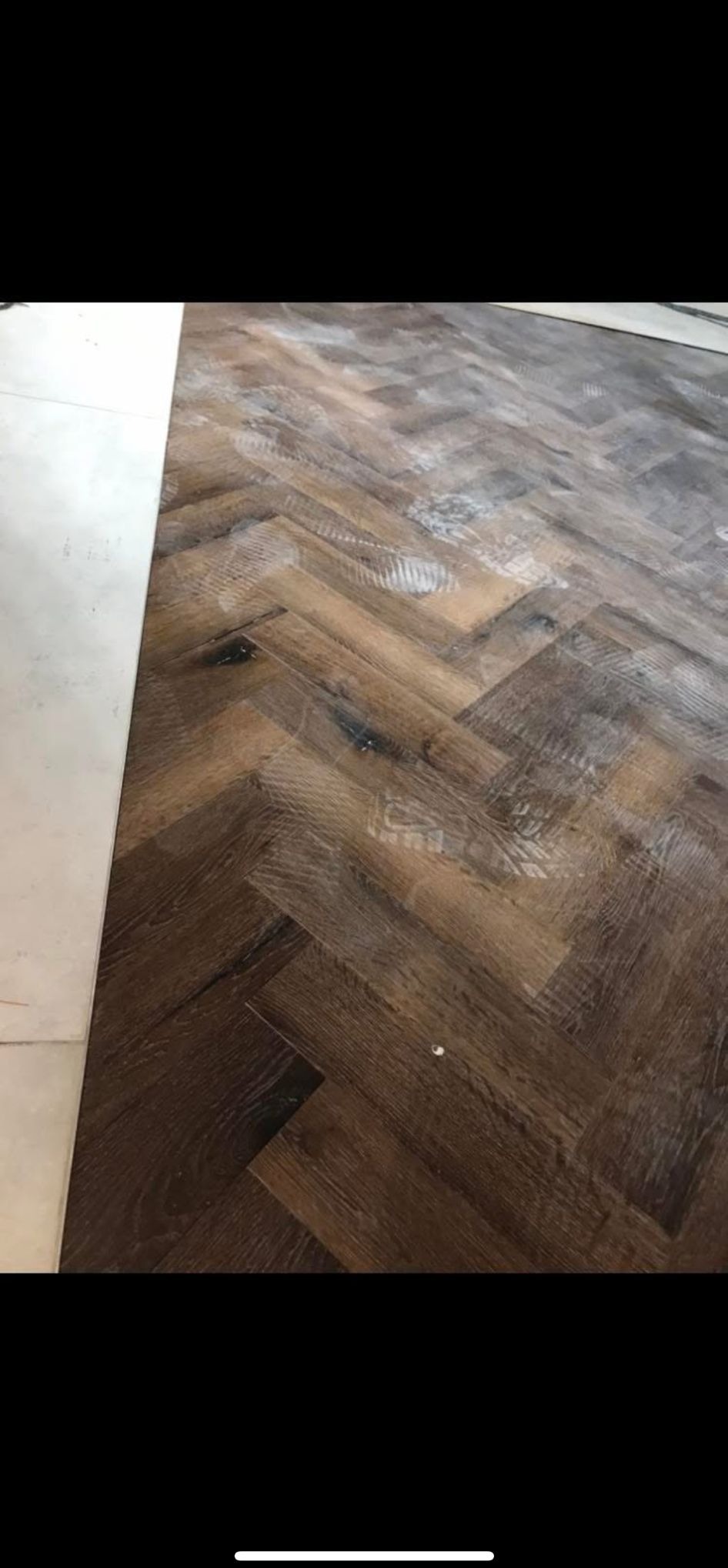 Ułożona podłoga z paneli w jodełkę, ciemne drewno z widocznymi słojami. Fragment białej listwy przypodłogowej. Widoczne ślady po montażu.
