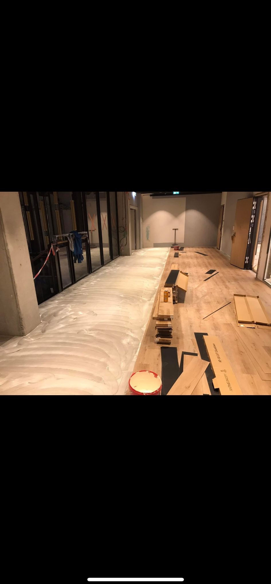 Połowa powierzchni z wylanym podkładem, druga z ułożonymi panelami. Widoczne narzędzia i materiały do układania podłogi. Etap prac wykończeniowych.