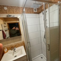 Hubert cap - Nowoczesna kabina prysznicowa z białymi płytkami w łazience z beżowymi akcentami. Widoczna umywalka z szafką i lustro z odbiciem osoby robiącej zdjęcie.