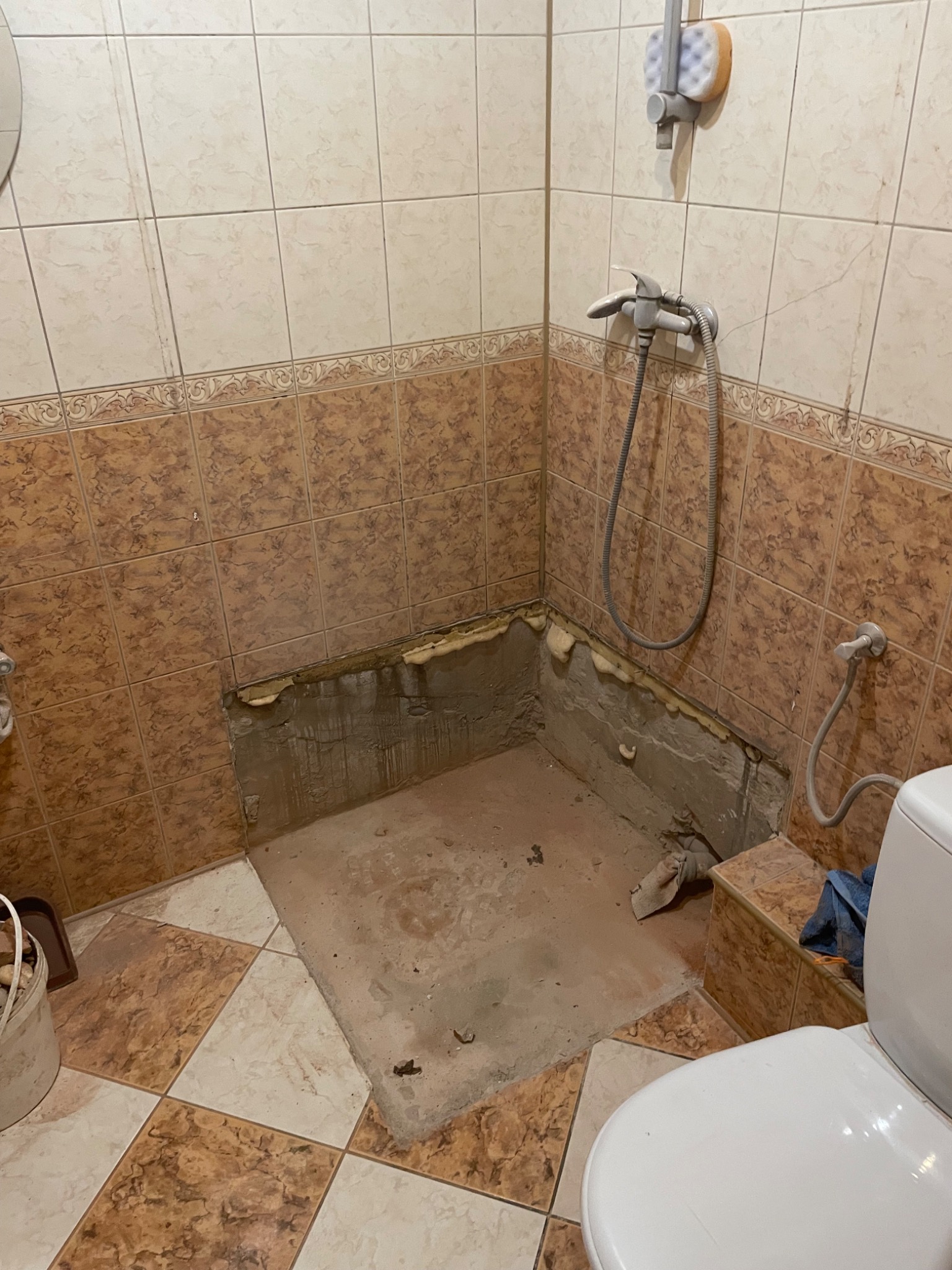 Demontaż płytek w rogu łazienki, widoczne ślady po usuniętych płytkach na ścianach i podłodze. Przygotowanie do dalszych prac wykończeniowych.