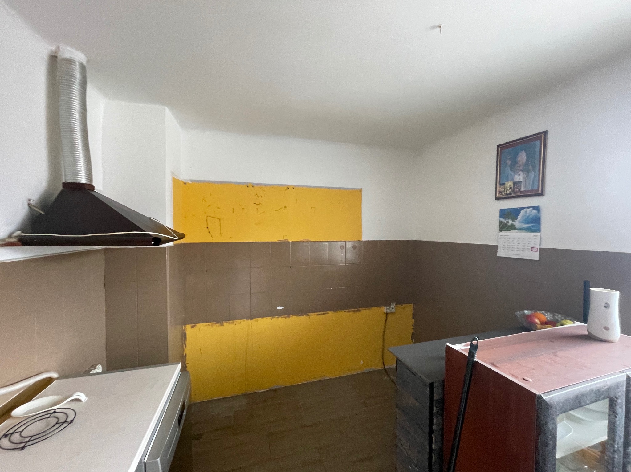 Kuchnia w trakcie demontażu płytek w Tarnogród. Widoczne odsłonięte fragmenty ściany i brązowe płytki. Okap kuchenny i meble częściowo widoczne.