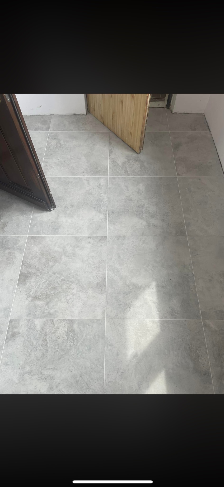 Ułożone szare płytki podłogowe z fugami, widoczne fragmenty dwóch par drzwi w surowym stanie, ściany przygotowane do malowania. Minimalistyczny efekt.