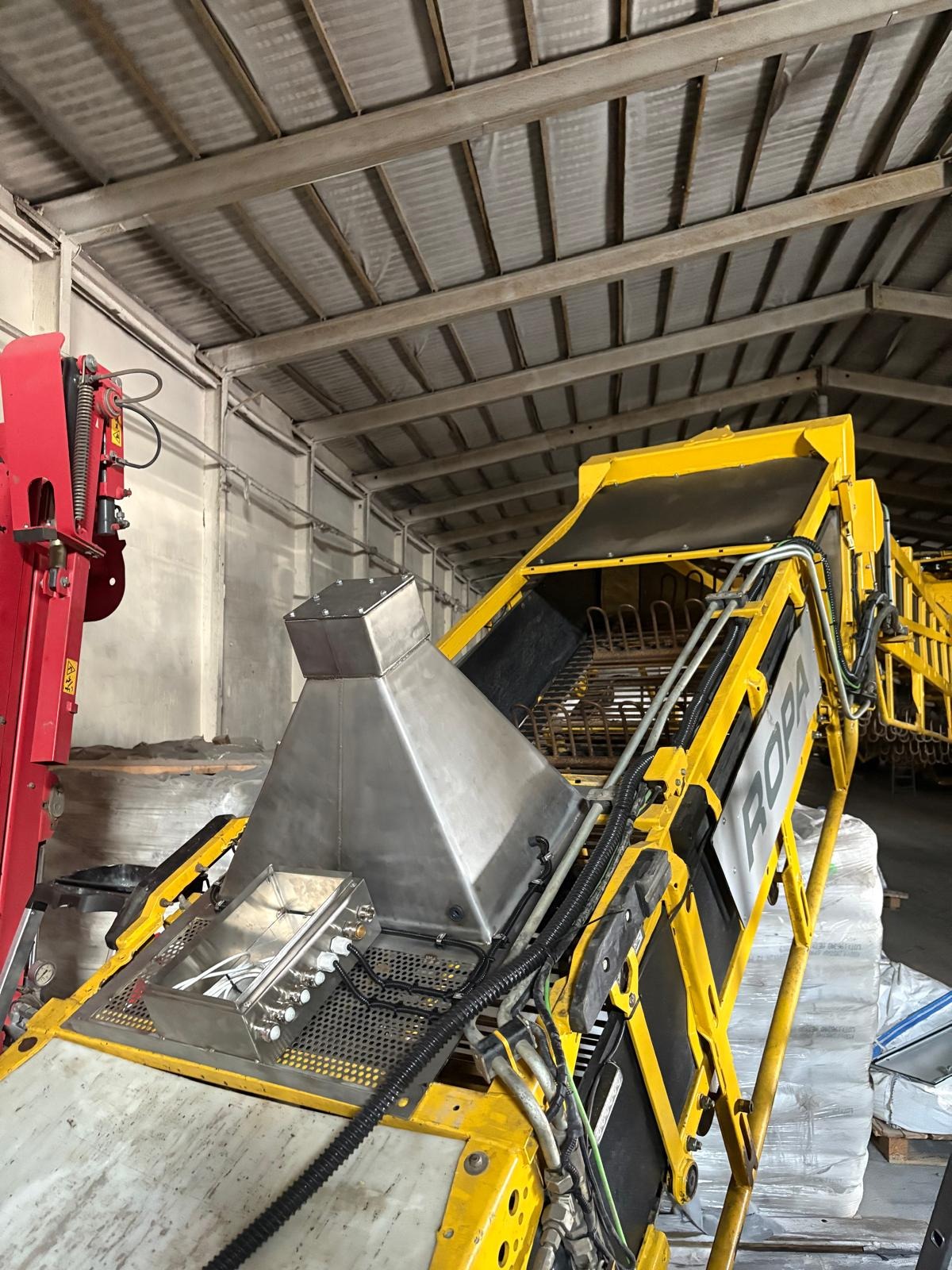 Żółto-srebrna maszyna rolnicza ROPA w hali, z widocznymi elementami metalowymi i hydraulicznymi. Perspektywa od dołu, ukazująca konstrukcję i detale urządzenia.