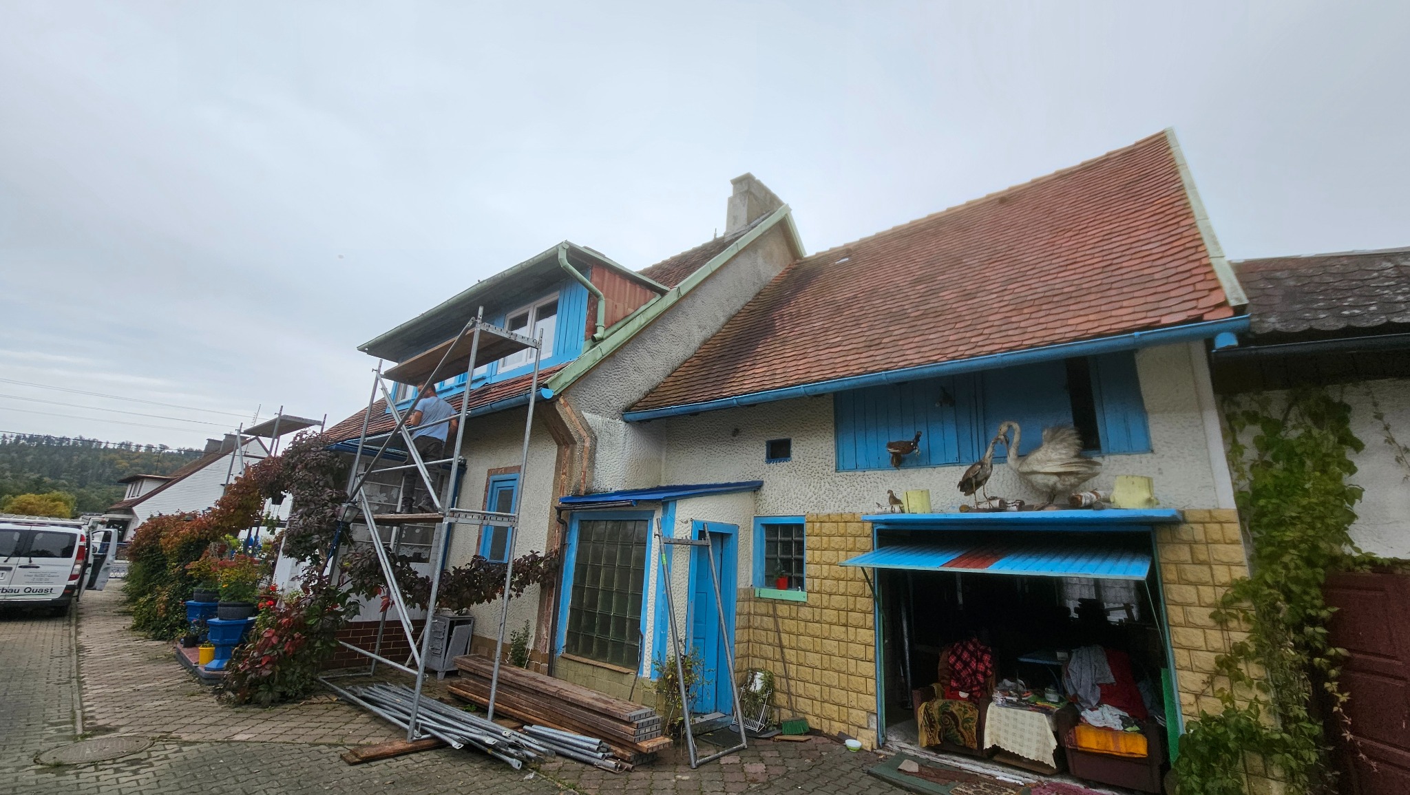Dom z rusztowaniem podczas prac elewacyjnych. Widoczne elementy dekoracyjne na budynku i narzędzia pracy. Ujęcie z dołu, pochmurne niebo w tle.