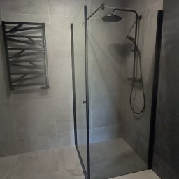 budujdomek - Nowoczesna łazienka z szarymi płytkami, kabiną prysznicową typu walk-in z czarnymi profilami i grzejnikiem drabinkowym o geometrycznym wzorze.