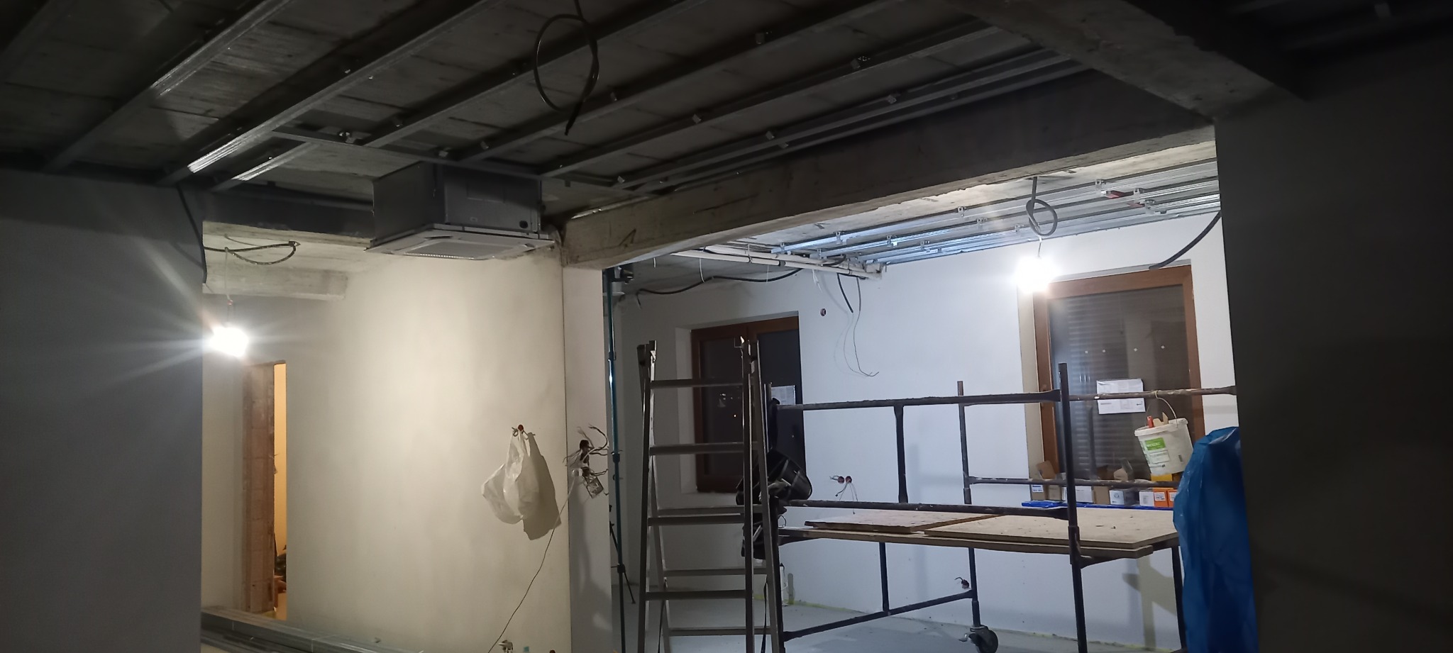 Wnętrze w trakcie prac wykończeniowych: widoczne rusztowanie, sufit podwieszany z instalacją, ściany przygotowane do malowania. Ujęcie z perspektywy podłogi.