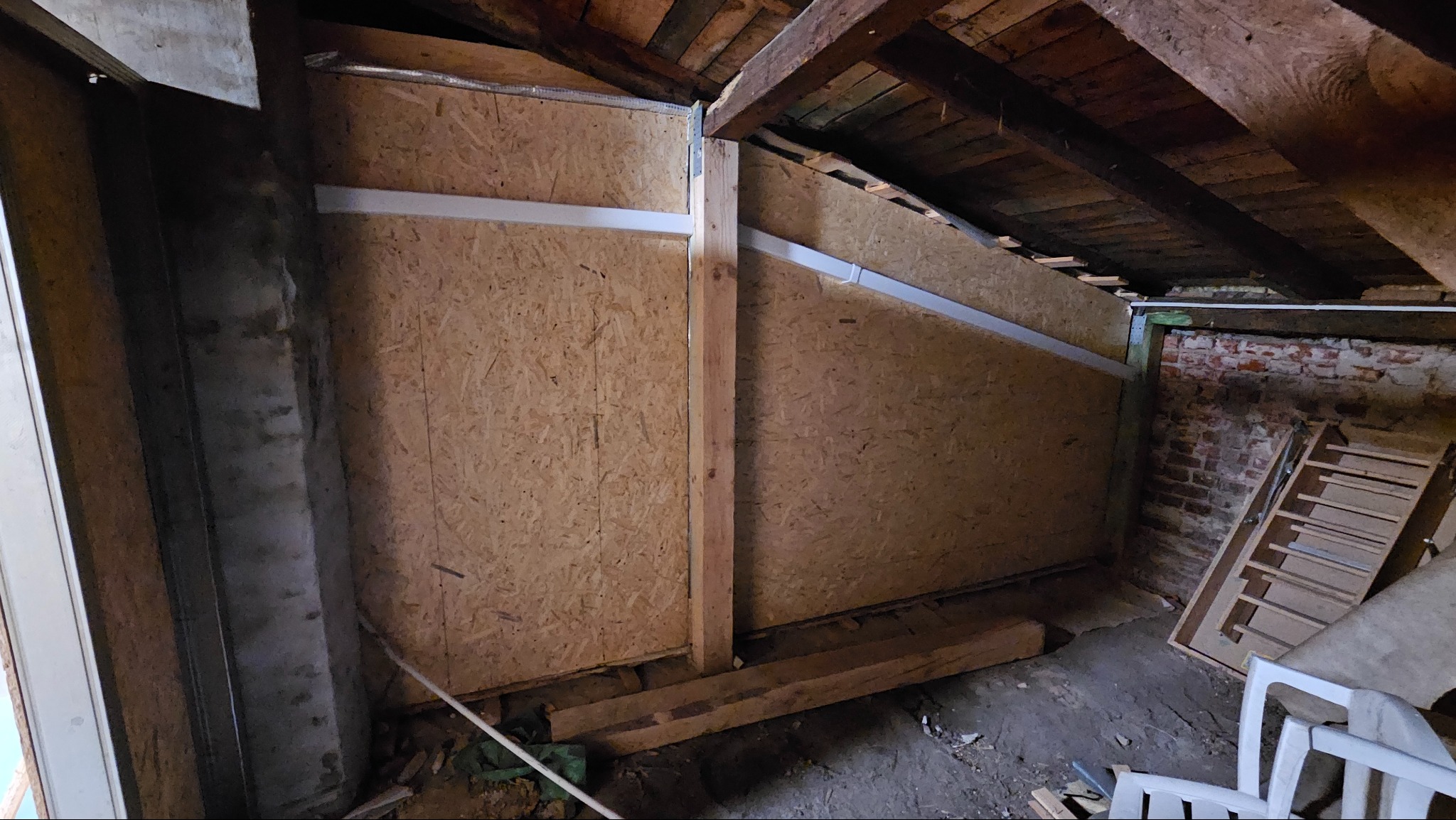 Płyty OSB na poddaszu, przymocowane do drewnianej konstrukcji. Widoczne elementy instalacji i fragment muru z cegły. Prace wykończeniowe na poddaszu.