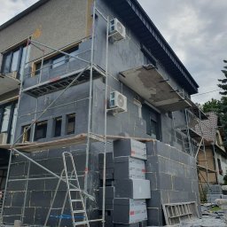 DARPROTECT DARIUSZ MARSZAŁEK - Ocieplanie elewacji budynku mieszkalnego styropianem grafitowym, widoczne rusztowania i drabina. Częściowo ocieplona ściana z zamontowanymi klimatyzatorami.