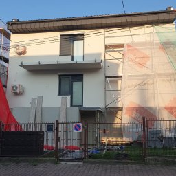 DARPROTECT DARIUSZ MARSZAŁEK - Dom jednorodzinny w trakcie ocieplania elewacji, widoczne rusztowania z siatką ochronną, częściowo otynkowana ściana, elementy klimatyzacji i ogrodzenie.
