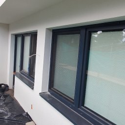 DARPROTECT DARIUSZ MARSZAŁEK - Biała elewacja budynku po malowaniu, widoczne okna z szarymi ramami i zasłonięte żaluzjami. Na podłożu folia ochronna, ślady prac malarskich.