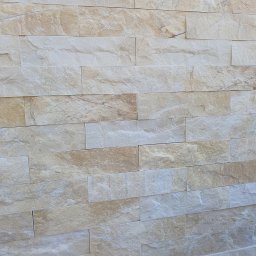 DARPROTECT DARIUSZ MARSZAŁEK - Ściana wykończona beżowymi, prostokątnymi płytkami imitującymi kamień naturalny, ułożonymi w regularny wzór z przesunięciem. Widoczna faktura i delikatne cieniowanie płytek.