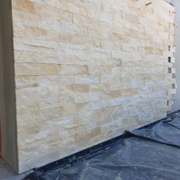 DARPROTECT DARIUSZ MARSZAŁEK - Ściana wykończona beżową okładziną kamienną, widoczne detale faktury i fugi. Częściowo ułożona, z widocznymi elementami montażowymi i folią ochronną u dołu.