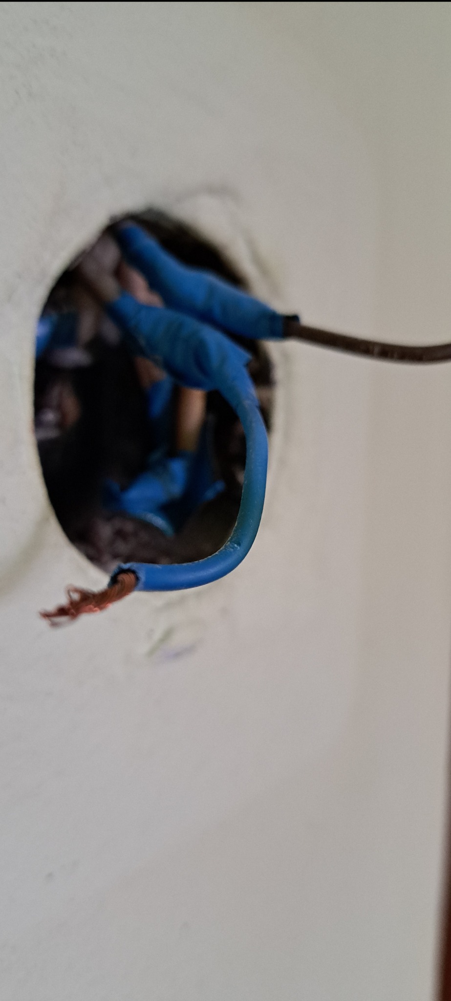 Niebieskie przewody elektryczne wystające z okrągłego otworu w ścianie, zabezpieczone izolacją. Widoczne detale instalacji po wymianie.