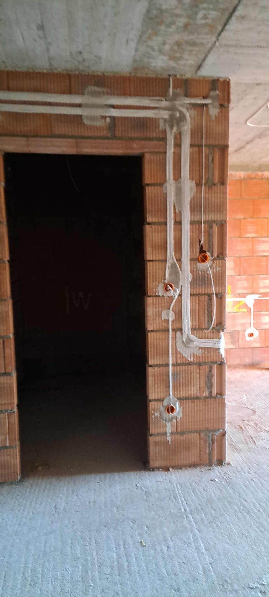 Instalacja elektryczna w trakcie montażu w nowym budynku z cegły. Widoczne kable i puszki elektryczne zamocowane na ścianie. Surowy stan wykończenia.