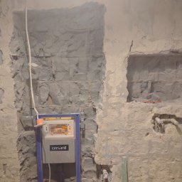 Usługi budowlane Daniel Suchecki - Montaż stelaża podtynkowego Cersanit w surowej łazience z wykuciami w ścianie. Widoczne instalacje wodne i kanalizacyjne. Prace przygotowawcze do wykończenia.