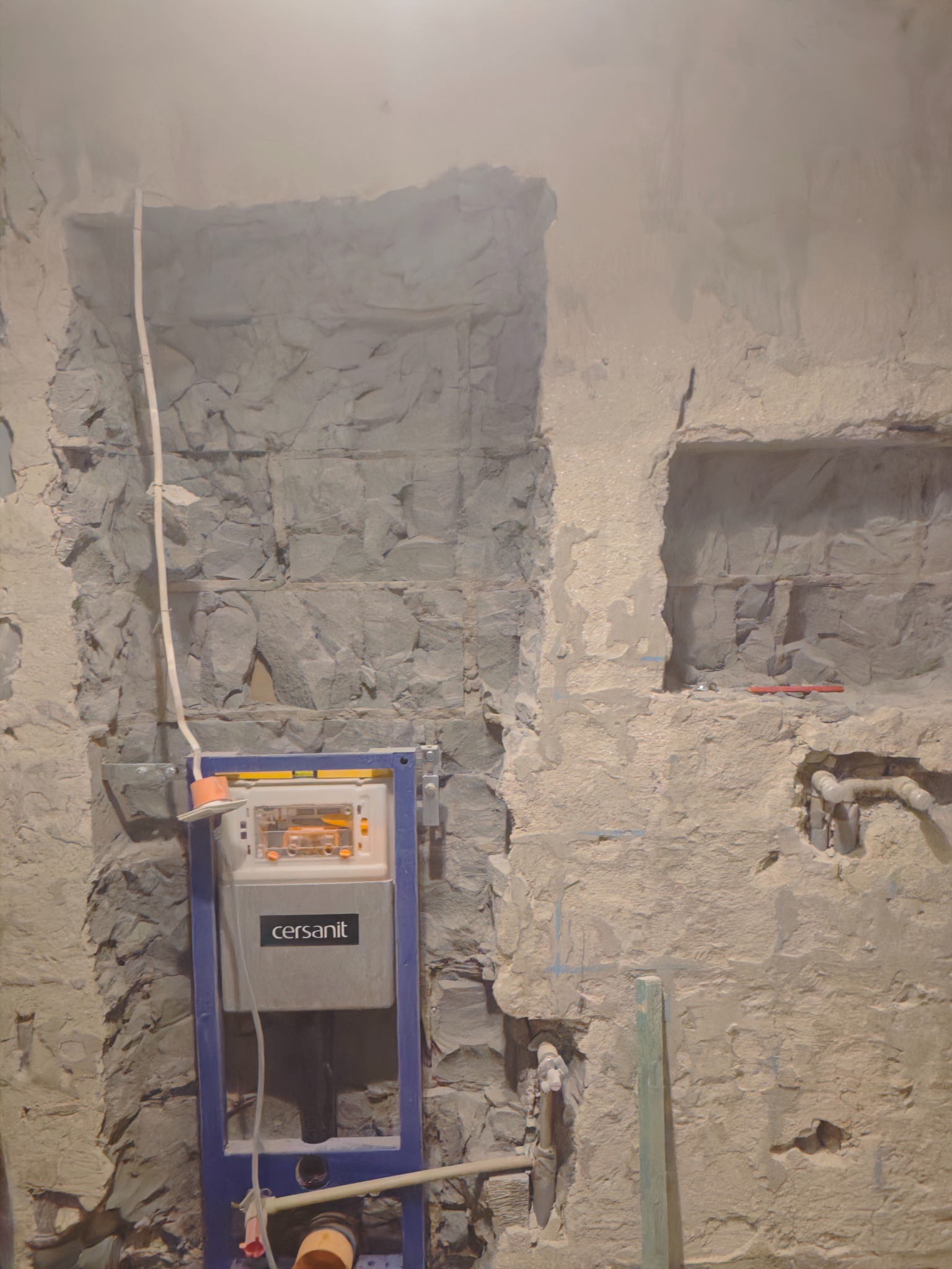 Montaż stelaża podtynkowego Cersanit w surowej łazience z wykuciami w ścianie. Widoczne instalacje wodne i kanalizacyjne. Prace przygotowawcze do wykończenia.