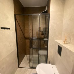 Mirosław Zdeb - Nowoczesna łazienka z kabiną prysznicową typu walk-in z czarnymi ramami, beżowymi płytkami i drewnianymi akcentami. Widoczna toaleta i dyfuzor zapachowy.