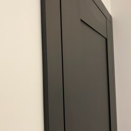 inż Mirosław Zdeb P.U - Ciemnoszare, minimalistyczne drzwi wewnętrzne z delikatnym frezem, zamontowane w jasnej ścianie. Ujęcie z bliska, akcentujące detale wykończenia.
