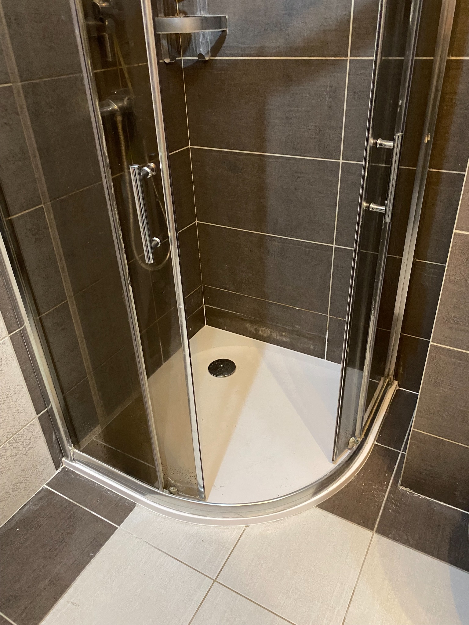 Nowoczesna kabina prysznicowa z ciemnymi płytkami i białą brodzikiem, widok z góry, chromowane wykończenia, po remoncie łazienki.