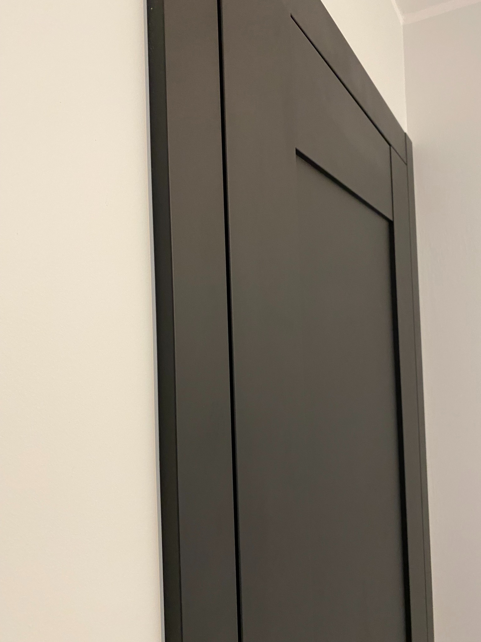 Ciemnoszare, minimalistyczne drzwi wewnętrzne z delikatnym frezem, zamontowane w jasnej ścianie. Ujęcie z bliska, akcentujące detale wykończenia.