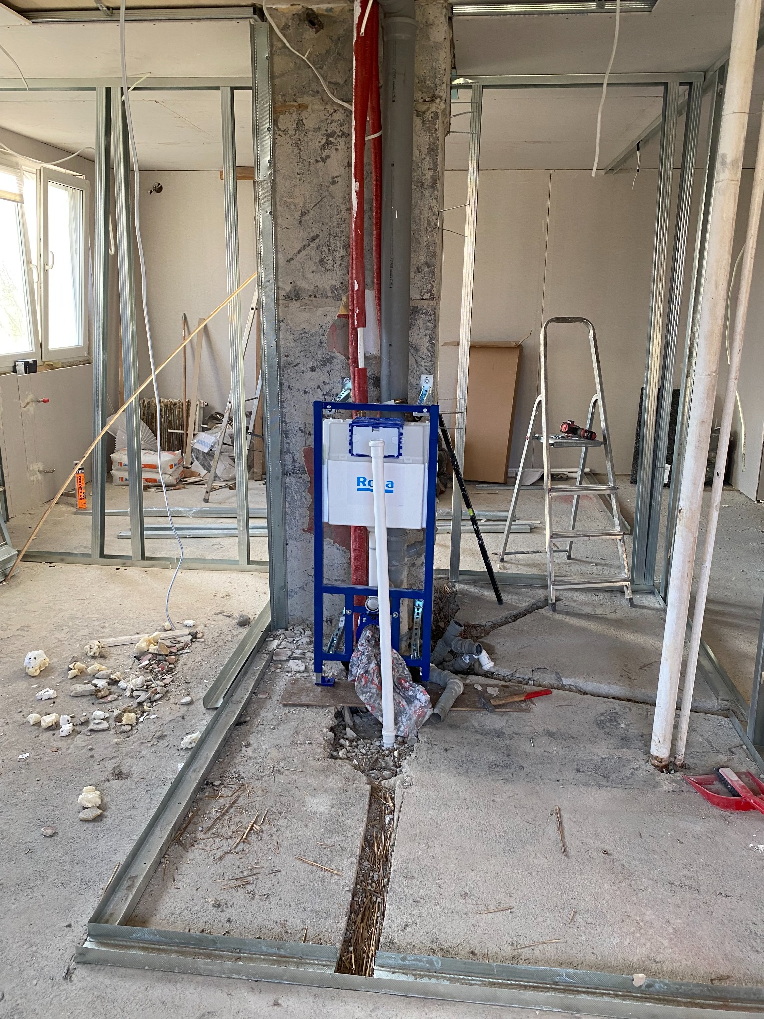 Wnętrze w trakcie remontu w Małogoszczu: widoczne stelaże ścianek działowych, instalacja sanitarna pod zabudowę i surowy beton. Etap prac wykończeniowych.