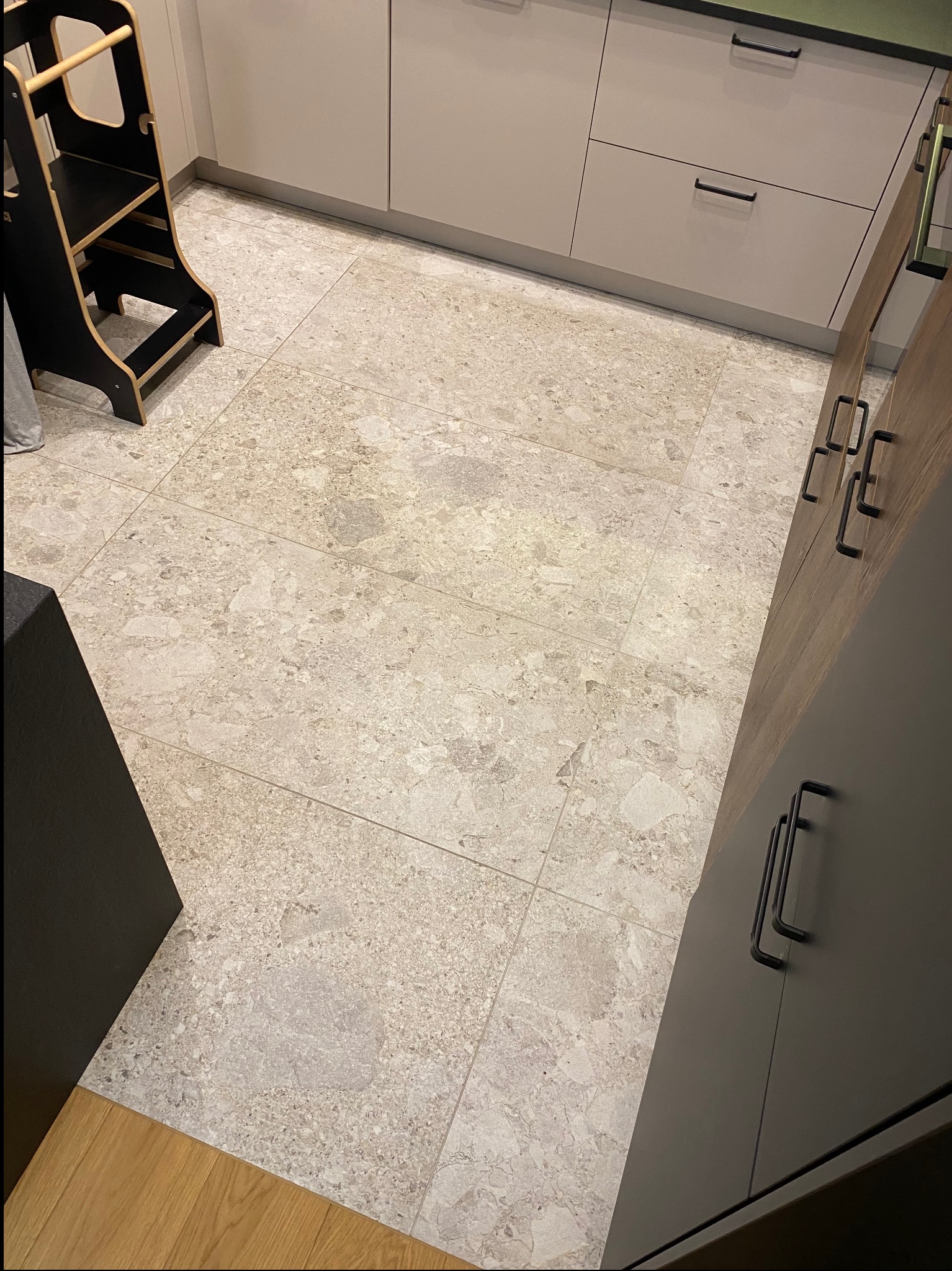 Jasne, marmurkowe płytki podłogowe w kuchni w Małogoszczu, z fragmentem szafek kuchennych i drabinką dla dziecka. Widok z góry, neutralne oświetlenie.