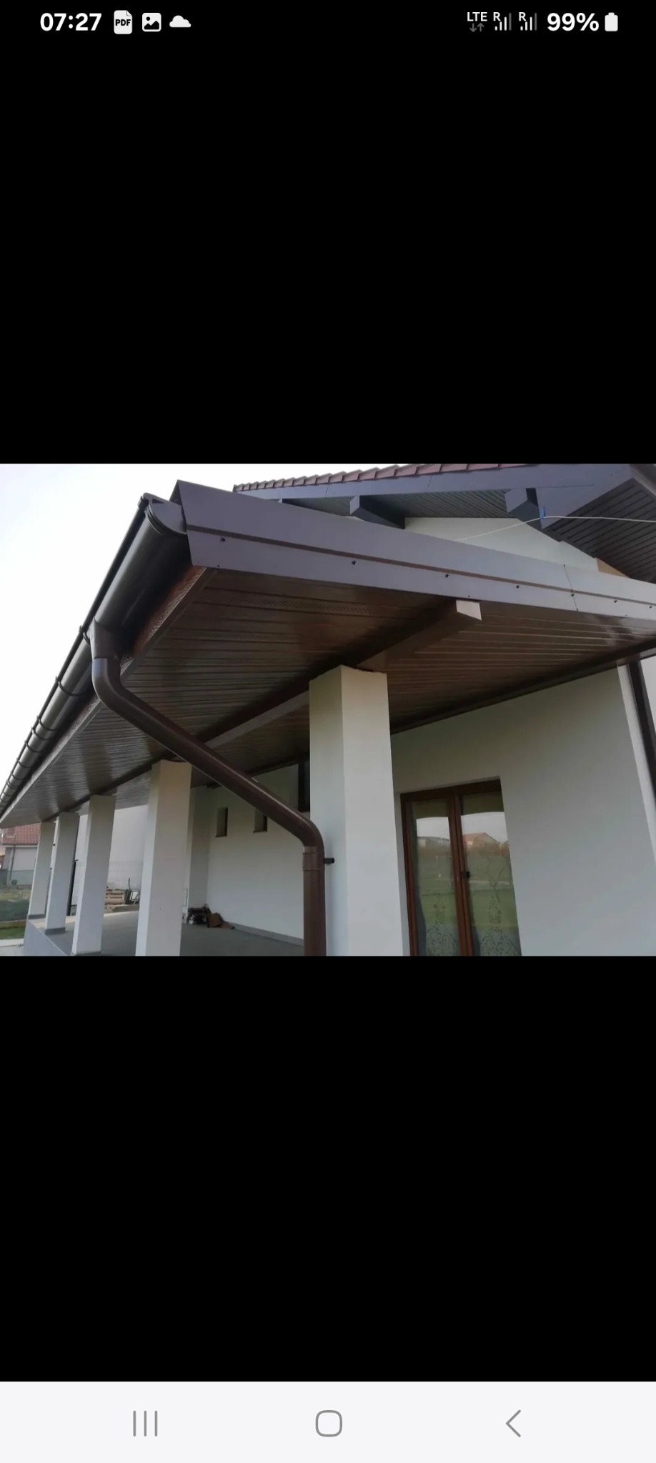 Brązowe rynny zamontowane na podbitce dachu domu z białymi kolumnami. Widok z dołu, ukazujący estetyczne wykończenie.