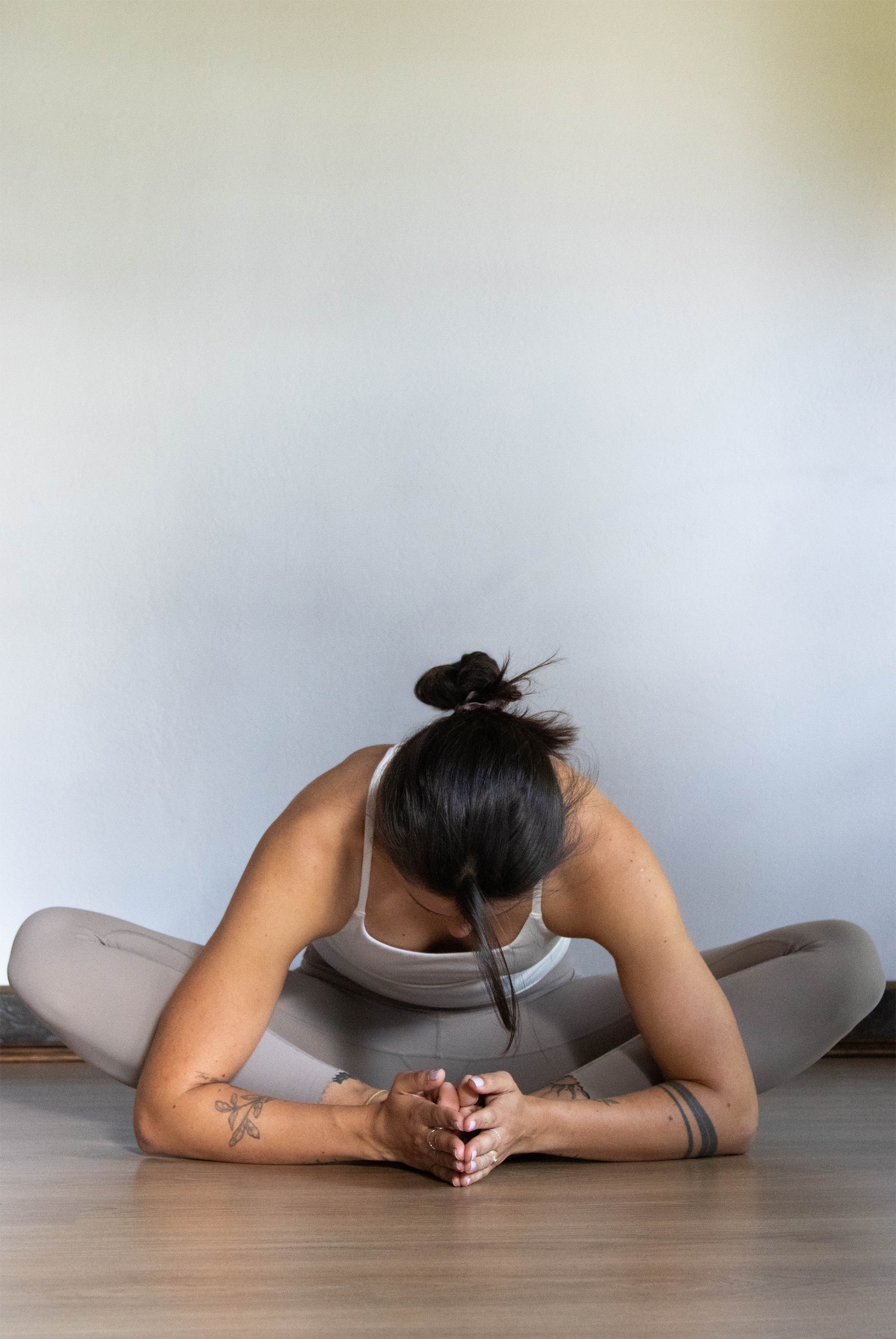 Kobieta w pozycji motyla podczas sesji jogi w Kobierzycach. Widoczne tatuaże na ramionach, włosy upięte w kok. Jasne legginsy i top. Minimalistyczne tło.